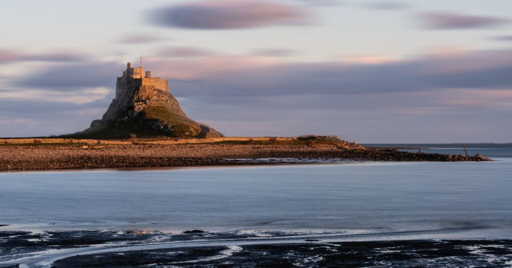 costa de Lindisfarne al atardecer con el castillo sobre una colina