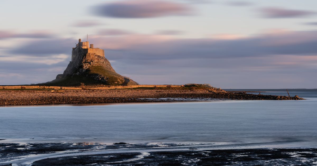 costa de Lindisfarne al atardecer con el castillo sobre una colina